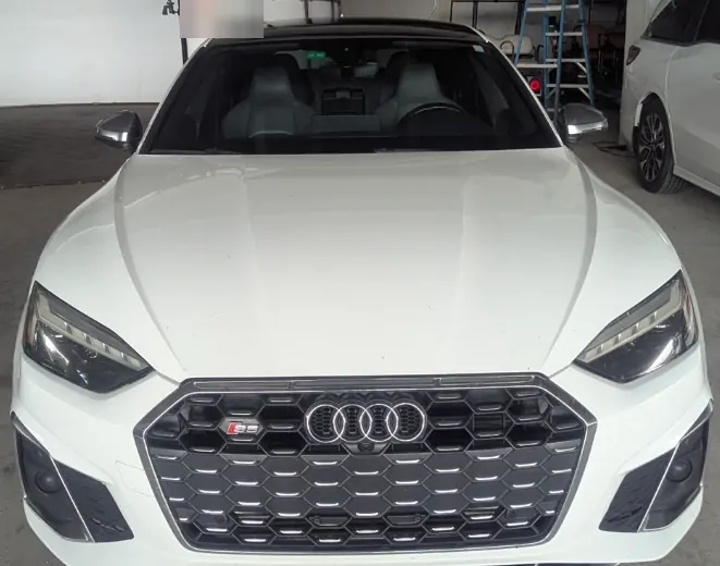 Front view of a white Audi S5 parked in a service bay for windshield replacement