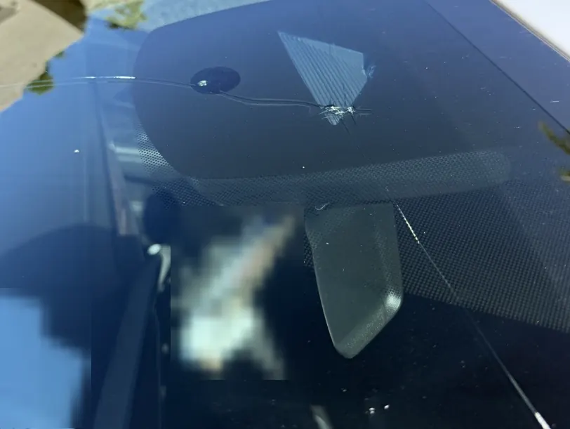 Cracked windshield with a rock chip and a crack running across the glass near the rearview mirror
