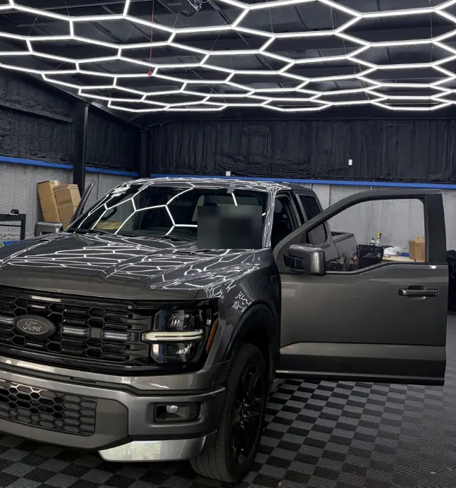 Dark gray Ford F-150 pickup with the driver's door open in a bay under hexagon LED lights