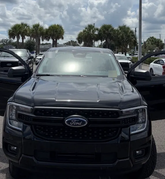 Black Ford Ranger pickup with both doors open in a parking lot lined with palm trees
